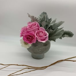 Pink roses arranged in a gray face-shaped vase with silvery foliage