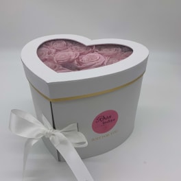 Heart-shaped white box filled with pink roses and tied with a white ribbon