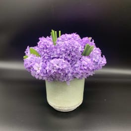 Purple flower arrangement in a pale green cylindrical vase