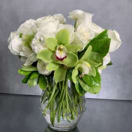White roses and green orchids arranged in a clear glass vase