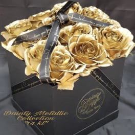 Gold roses arranged in a black gift box with a ribbon.