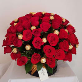 Red roses arranged with gold-wrapped chocolates in a black box.