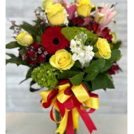 Bouquet of yellow and red flowers with a red ribbon in a glass vase