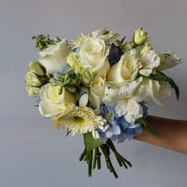 Handheld bouquet of white roses, blue hydrangea, and pale daisies