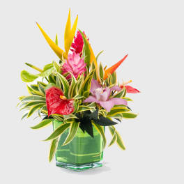 Tropical flower arrangement in a green glass vase with pink and yellow blooms