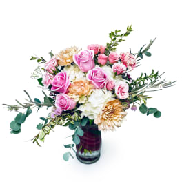 Pink roses and cream flowers in a glass vase with trailing greenery