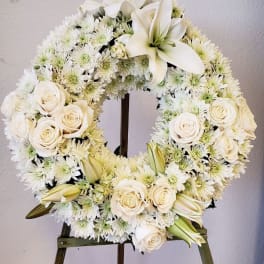 White floral wreath on an easel with roses, lilies, and daisies