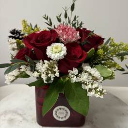Red roses and white filler flowers in a burgundy square vase