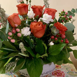 Orange roses and white carnations in a white vase with greenery and pink berries