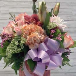 Pink and peach floral arrangement in a vase with a lavender bow