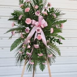 Standing floral spray with pink carnations and a pink ribbon on an easel