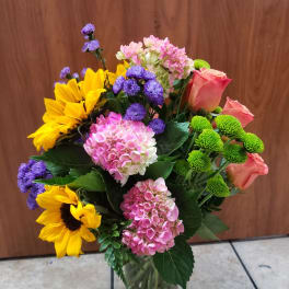 Mixed bouquet in a glass vase with sunflowers, pink roses, and hydrangeas