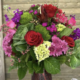 Mixed bouquet of red roses, pink blooms, and purple flowers in a textured vase