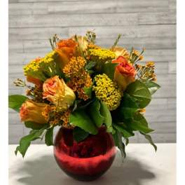 Orange roses in a red glass vase with yellow filler flowers