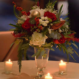 Red and white rose centerpiece with holiday greens in a clear vase, surrounded by three votive candles