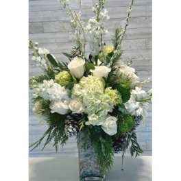 White floral arrangement in a tall glass vase with pinecones and greenery