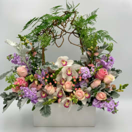 Pink roses and white orchids in a white container with an arching vine frame