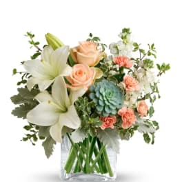 Peach roses and white lilies in a clear glass vase