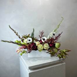 Long floral arrangement with white and burgundy roses in a white rectangular vase