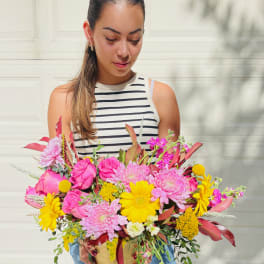 Woman holding a large pink and yellow flower arrangement in a gold container