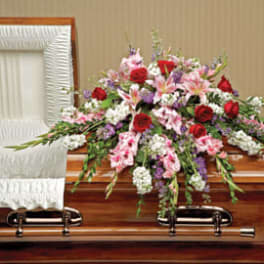 Casket spray of red roses, pink lilies, and mixed flowers on a wooden casket