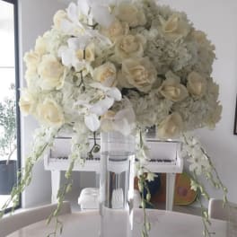 White floral arrangement in a clear glass vase with trailing orchids