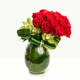 Red rose bouquet with green orchids in a glass vase