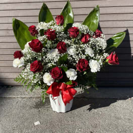 Red roses and white carnations in a white vase with a red ribbon