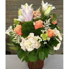 Peach roses and white lilies arranged in a brown vase