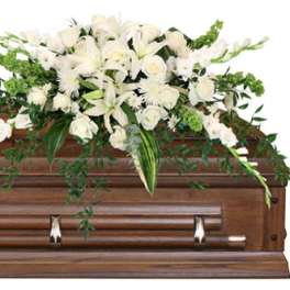 White floral casket spray with lilies and roses on a wooden casket
