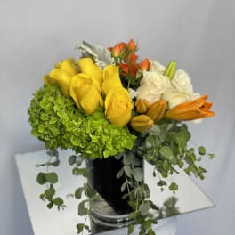 Bouquet of yellow, white, and orange roses with green hydrangea in a black vase