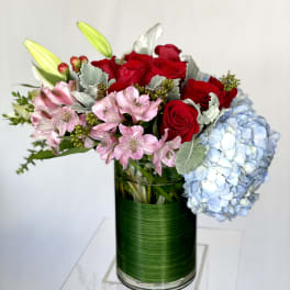 Bouquet of red roses, pink lilies, and blue hydrangea in a glass vase