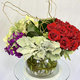 Red roses and purple flowers in a glass bowl vase with pale foliage