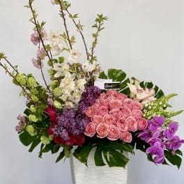 Large mixed floral arrangement in a white vase with pink, purple, and white blooms
