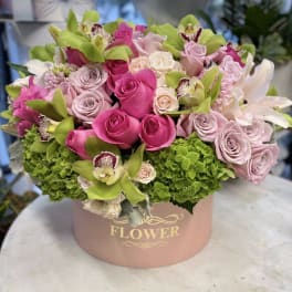 Pink and lavender roses with green orchids in a round box