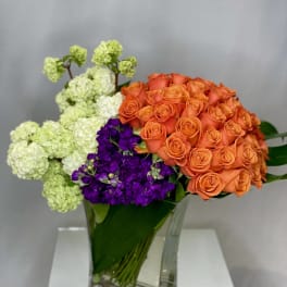 Orange roses and purple flowers in a clear glass vase with pale green blooms