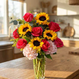 Tall vase of yellow sunflowers, pink roses, and pale hydrangeas on a wooden kitchen island