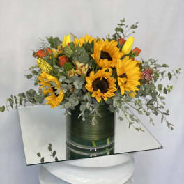 Sunflowers and orange roses in a green glass vase