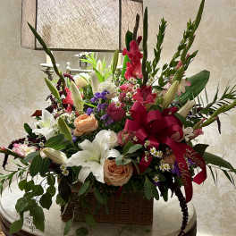 Large mixed flower arrangement in a wicker basket with a red ribbon