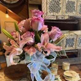 Pink lilies and roses arranged in a vase with a blue ribbon bow