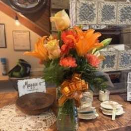 Orange and yellow floral arrangement in a glass vase with a ribbon