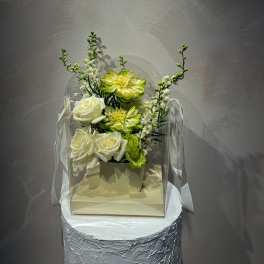 White and lime floral arrangement in a clear box with ribbon handles