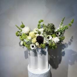 White and green floral arrangement in a tall white vase