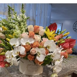Mixed bouquet of white orchids, peach roses, yellow lilies, and red anthuriums in a white box
