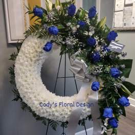 White floral wreath with blue roses on a stand and silver ribbon