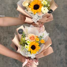 Two hand-tied bouquets with sunflowers and roses wrapped in blush paper