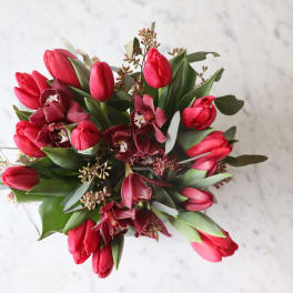 Bouquet of red tulips and dark orchids with greenery