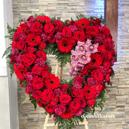 Heart-shaped floral wreath of red roses and pink orchids on an easel