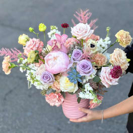 Pastel mixed bouquet in a pink vase with roses, peonies, and orchids