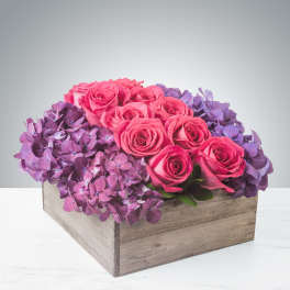 Low arrangement of hot pink roses and purple hydrangeas in a rustic wooden box
